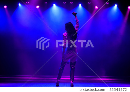 Cool singer with microphone on bright backlit stage in bright blue lights 83341372