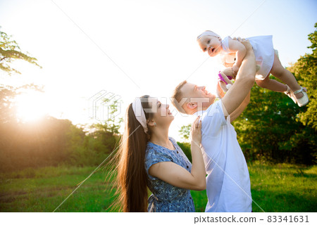 Happy family playing on the grass in the park in the evening. 83341631