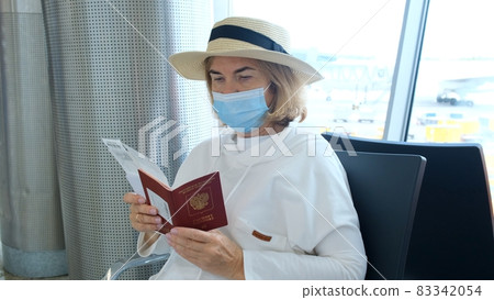 adult Female wearing a hat and a protective mask sits at the check-in counters in the airport 83342054