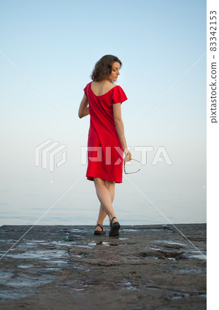 Young girl in red dress on the sea and blue background, summertime, travelling concepts 83342153