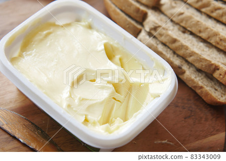 salted butter in a plastic container and breads on table  83343009