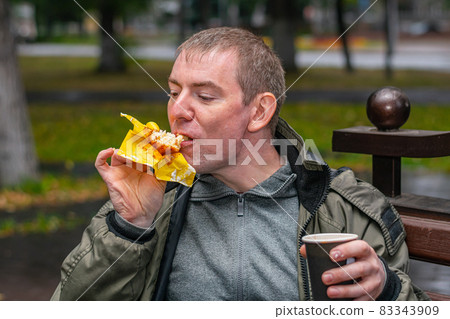 A man in the park enjoying a sweet bun 83343909
