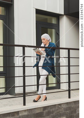 Smiling muslim girl using digital tablet, browsing Internet or social networks outdoor Smiling muslim girl using digital tablet, browsing Internet or social networks outdoor 83344744