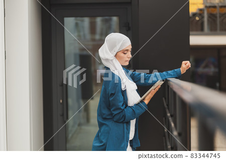 Young asian muslim woman in head scarf smile with mobile tablet and copy space Young asian muslim woman in head scarf smile with mobile tablet and copy space 83344745