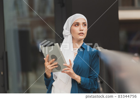 Beautiful Asian businesswomen wearing hijab using her tablet at outdoor. 83344756