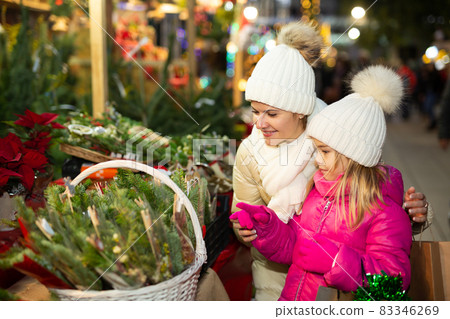 Happy mom with daughter buy spruce twigs for Christmas celebration 83346269