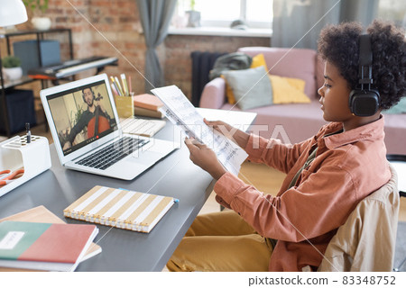 Cute boy with papers with musical notes sitting in front of laptop 83348752