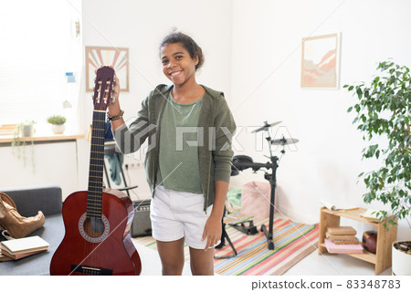 Happy schoolgirl with guitar standing in the center of domestic room Happy schoolgirl with guitar standing in the center of domestic room 83348783