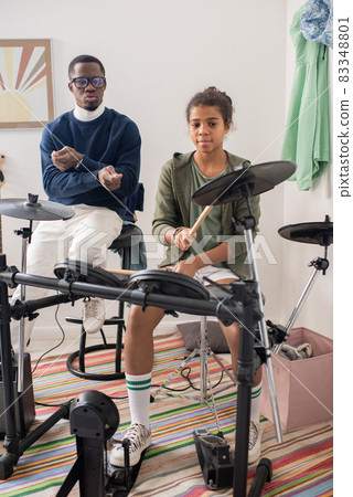 Cute schoolgirl hitting cymbal of drumkit during home repetition Cute schoolgirl hitting cymbal of drumkit during home repetition 83348801
