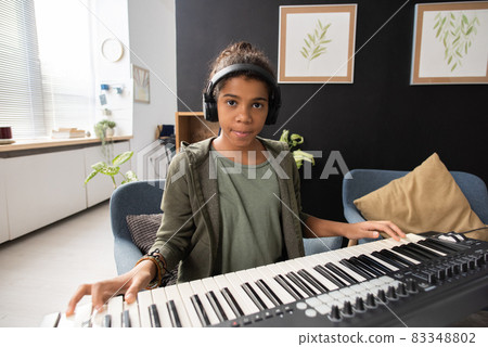 Serious African-American schoolgirl sitting by piano keyboard Serious African-American schoolgirl sitting by piano keyboard 83348802