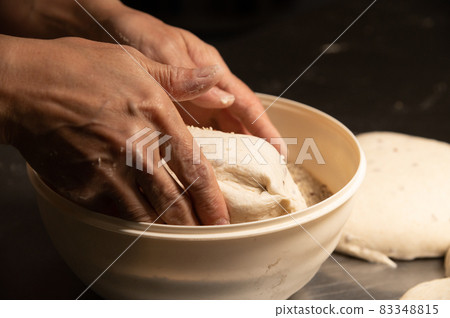 close-up of a baker's female hands dipping dough into a bowl of seeds and cereals before baking artisan bread at a home bakery close-up of a baker's female hands dipping dough into a bowl of seeds and cereals before baking artisan bread at a home bakery 83348815