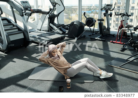 Young pretty sportswoman doing sit-ups with side turns Young pretty sportswoman doing sit-ups with side turns 83348977