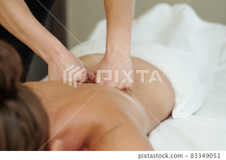 Hands of masseuse pressing punches against back of young woman 83349051