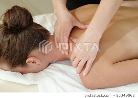 Hands of masseuse touching shoulder of young woman during beauty procedure Hands of masseuse touching shoulder of young woman during beauty procedure 83349068