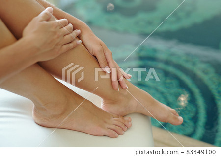 Hands of barefoot female on her legs against water Hands of barefoot female on her legs against water 83349100