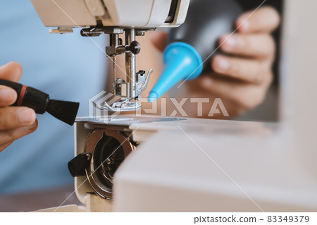 A young woman cleaning a sewing machine. A young woman cleaning a sewing machine. 83349379