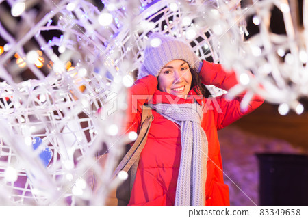 Winter holiday season. Christmas, New Year concept. Funny happy woman spend time having fun near illuminated and decorated showcase on city street. 83349658