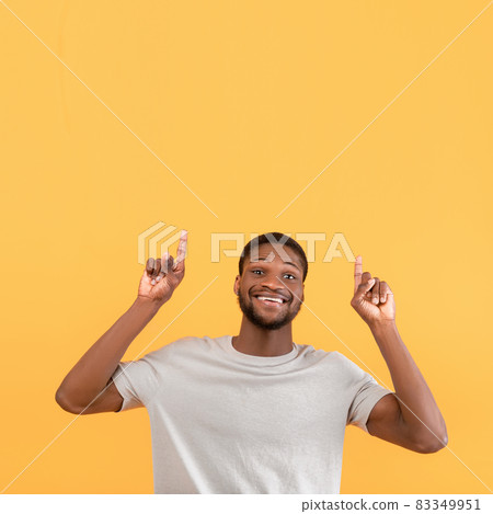 Overjoyed black guy pointing fingers up at free space and smiling to camera, standing over yellow background Overjoyed black guy pointing fingers up at free space and smiling to camera, standing over yellow background 83349951