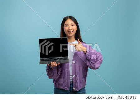Online educational courses. Cheerful asian female student pointing at laptop with blank screen, blue studio background Online educational courses. Cheerful asian female student pointing at laptop with blank screen, blue studio background 83349985