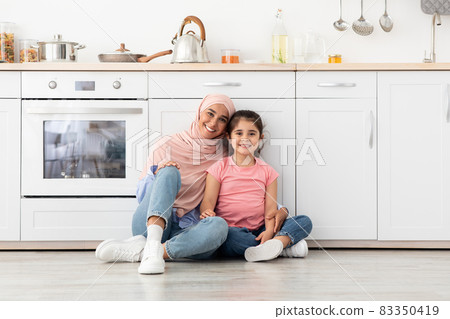 Happy Muslim Family Mother And Little Daughter Relaxing On Floor In Kitchen Happy Muslim Family Mother And Little Daughter Relaxing On Floor In Kitchen 83350419