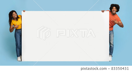 Happy african american couple pointing at horizontal blank placard Happy african american couple pointing at horizontal blank placard 83350431
