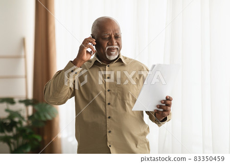 Mature Black Male Talking On Phone Holding Paper Standing Indoors 83350459