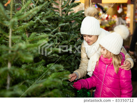 Pleasant woman with daughter buying Christmas tree in market Pleasant woman with daughter buying Christmas tree in market 83350712