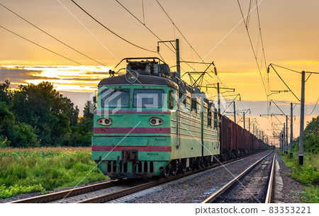 Electric locomotive hauling a cargo train at sunset 83353221