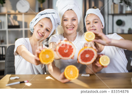 Two sisters with mother using slices of citrus for skin care 83354876
