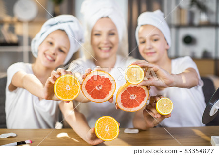Woman with two daughters holding slices of citrus at table 83354877
