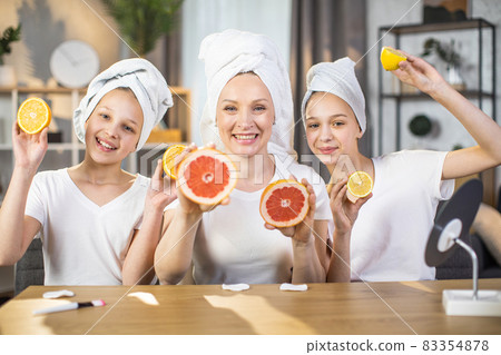 Two sisters with mother holding slices of citrus in hands 83354878