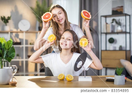 Two sisters posing at home with slices of citrus in hands 83354895