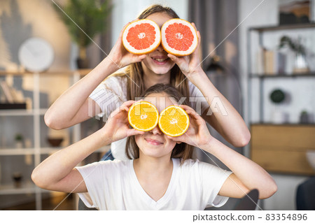 Two happy sisters hiding eyes under slices of citrus Two happy sisters hiding eyes under slices of citrus 83354896