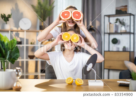 Two happy sisters hiding eyes under slices of citrus 83354900