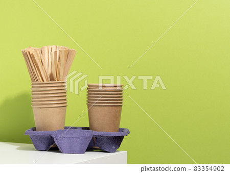 stack of brown disposable paper cups and a stand on a white table, green background. Utensils for takeaway drinks, zero waste stack of brown disposable paper cups and a stand on a white table, green background. Utensils for takeaway drinks, zero waste 83354902
