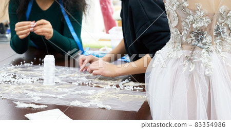 Mannequin with a wedding dress is in the tailor's shop. Dressmaker working in atelier. 83354986