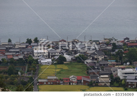 A view of the seaside town with many private houses, fields, parks, roads and boats seen from a hill 83356069