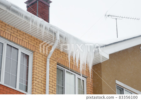 Big icicles on the roof of a townhouse on a snowy winter day among thaw 83356100