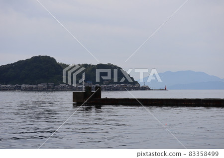 A landscape of towns such as boathouses and private houses, a peninsula, a red lighthouse, a hazy mountain, and a cloudy sky that can be seen behind a jetty in the calm sea A landscape of towns such as boathouses and private houses, a peninsula, a red lighthouse, a hazy mountain, and a cloudy sky that can be seen behind a jetty in the calm sea 83358499