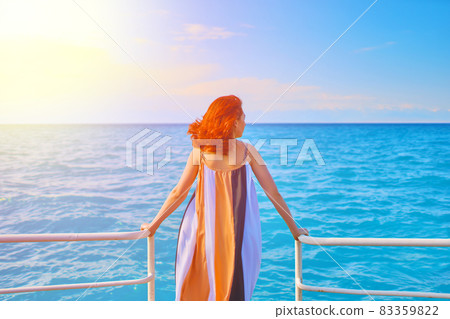 Cute girl in flowing long dress stands on edge of sea pier. 83359822