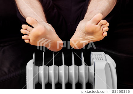 Electric oil heater with man who warms his feet. Electric oil heater with man who warms his feet. 83360356