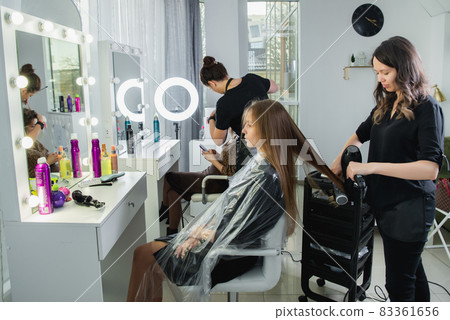 Close up of hairdressers hands drying long blond hair with blow dryer and round brush Close up of hairdressers hands drying long blond hair with blow dryer and round brush 83361656