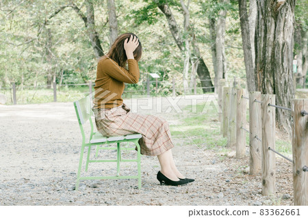 A woman holding her head on the bench, a person who is worried alone in the park A woman holding her head on the bench, a person who is worried alone in the park 83362661