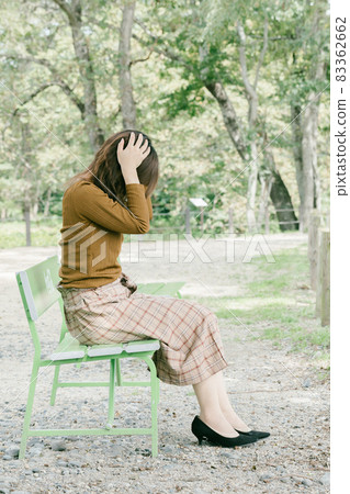 A woman holding her head on the bench, a person who is worried alone in the park A woman holding her head on the bench, a person who is worried alone in the park 83362662