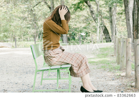 A woman holding her head on the bench, a person who is worried alone in the park 83362663
