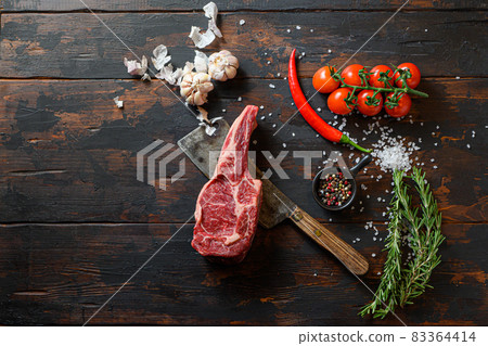 Raw Delmonico steak on meat cleaver. Organic farm marbled prime black angus beef. Dark wooden background. top view. With seasonings, peppercorns, chilie rosemary,salt,garlic. space for text. Copyspace 83364414