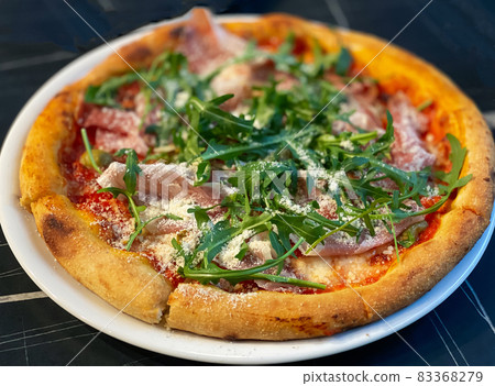 Close-up on a restaurant table pizza with prosciutto, arugula and parmesan cheese 83368279