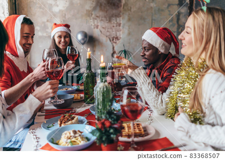 People celebrating sitting at the table, clinking glasses. Christmas or New Year eve. People celebrating sitting at the table, clinking glasses. Christmas or New Year eve. 83368507
