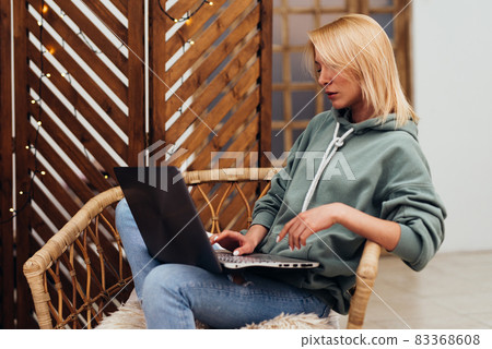 Young woman working on laptop while sitting in chair at home. Young woman working on laptop while sitting in chair at home. 83368608