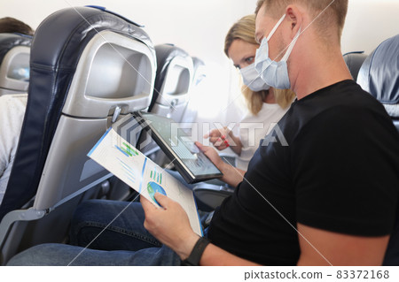 Man and woman in protective medical masks flying in airplane and discussing diagram on documents 83372168